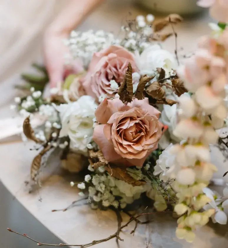 A bouquet featuring pale pink and white roses, baby's breath, and dried brown leaves arranged on a light surface.