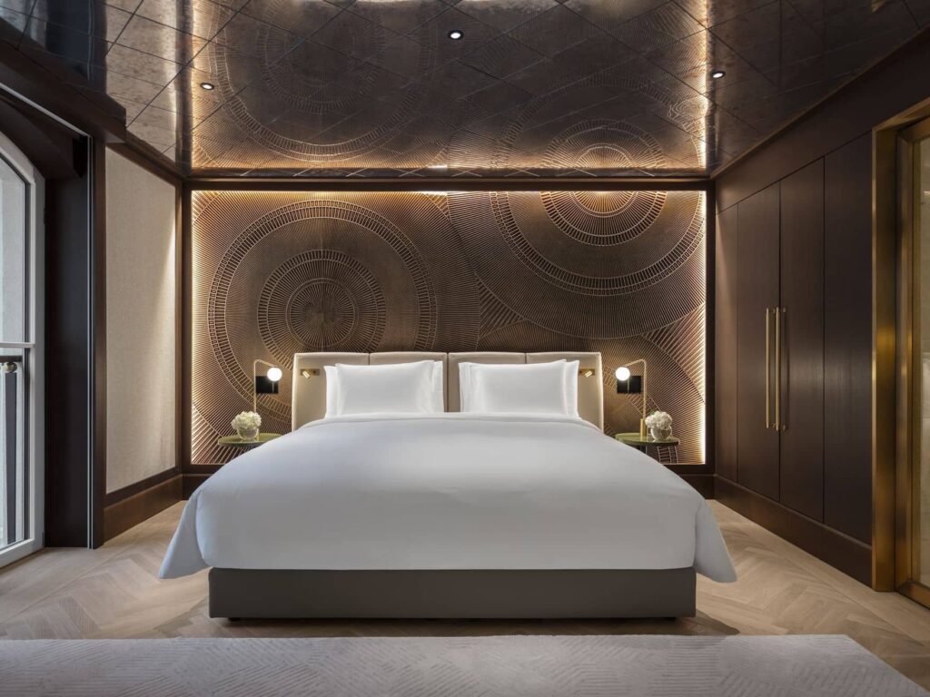 Modern hotel room featuring a double bed with white linens, decorative wall paneling, ambient lighting, built-in wardrobes, and elegant Palais Floor for a sophisticated touch.