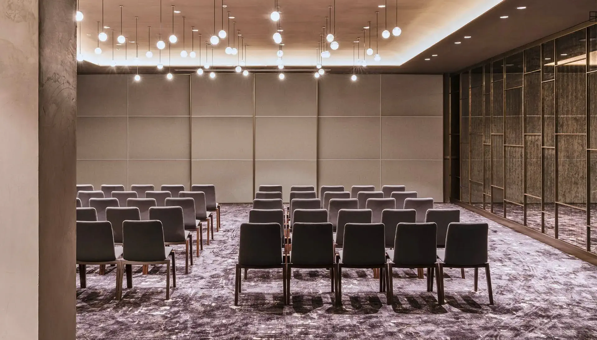 Filas de sillas vacías frente a una pared en blanco en una moderna sala de conferencias, perfecta para celebrar eventos sociales, con lámparas de techo colgantes y moqueta estampada.