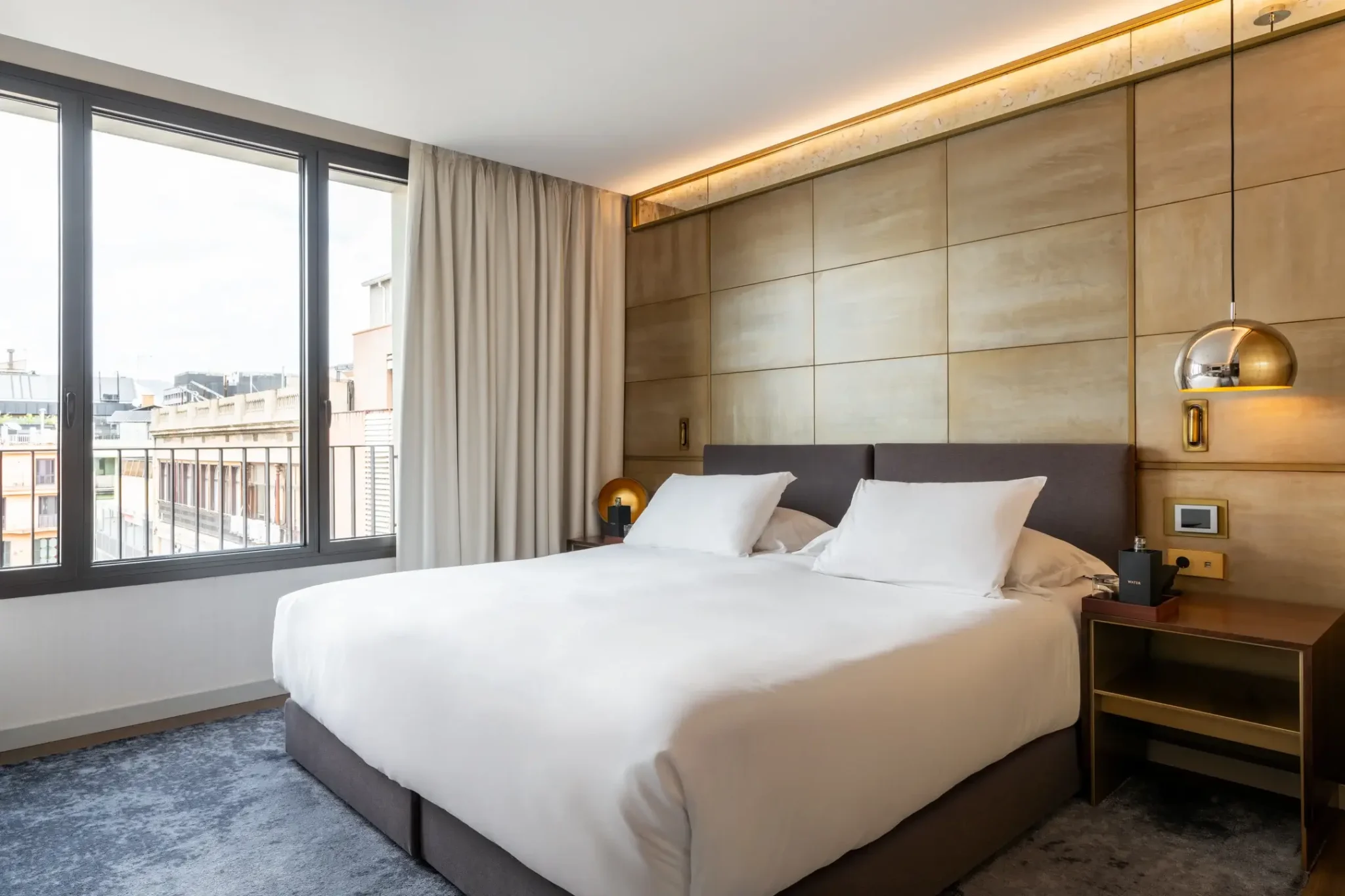 Habitació d'hotel moderna de la Habitació Gallery amb un llit gran, dues tauletes de nit amb làmpades, una finestra del terra al sostre amb cortines i una paret decorativa encoixinada darrere del capçal.