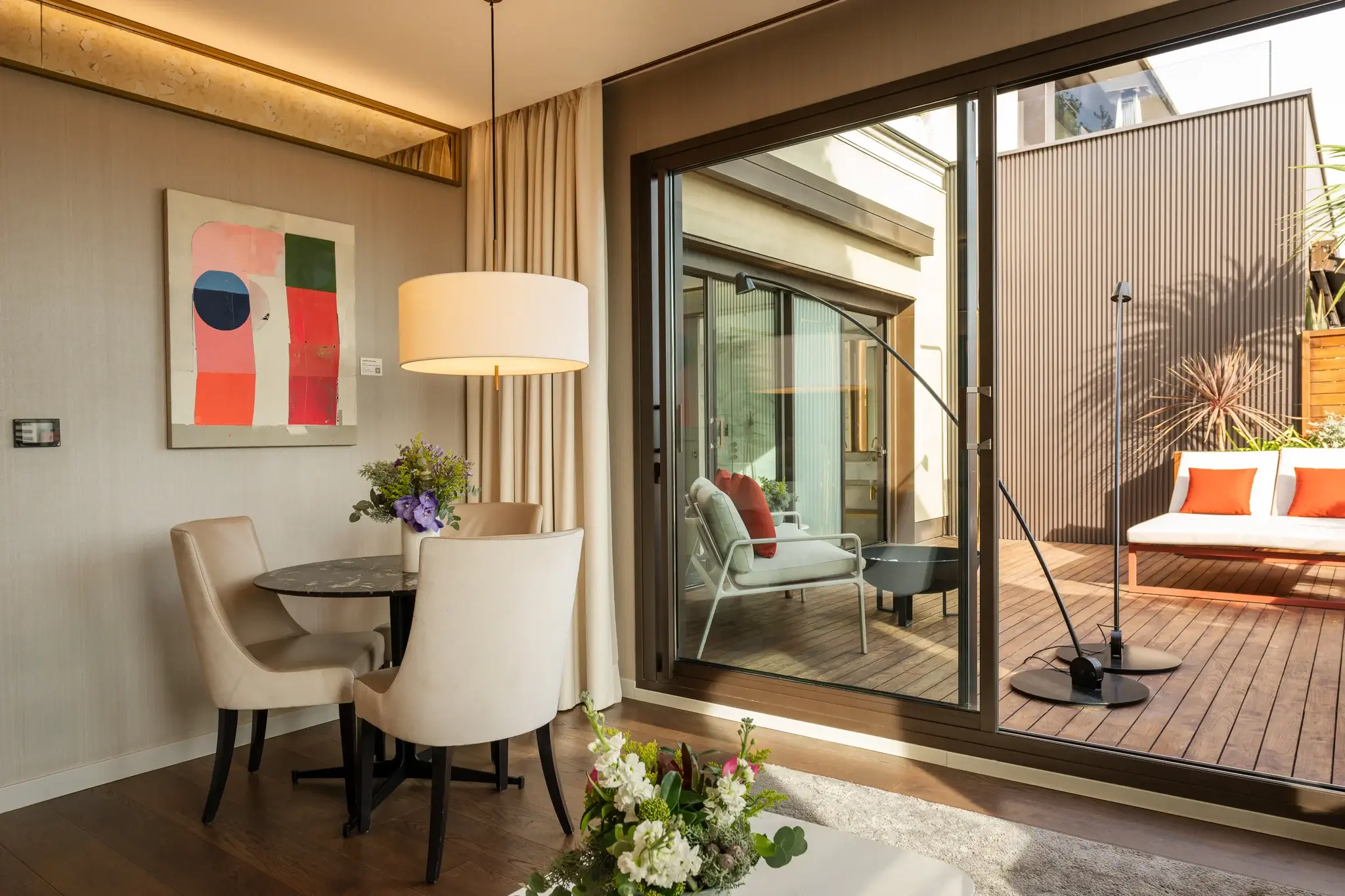 Menjador modern amb una petita taula rodona i cadires al costat de grans portes corredisses de vidre, que condueixen a un pati de fusta amb seients a l'aire lliure, un espai acollidor que es troba a la nostra exclusiva Suite Àtic amb dues habitacions.