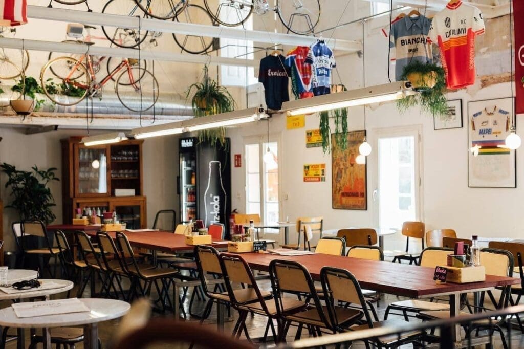 A spacious café, Eroica Caffè features long wooden tables, yellow chairs, hanging bicycles, cycling jerseys, and natural light streaming through large windows.
