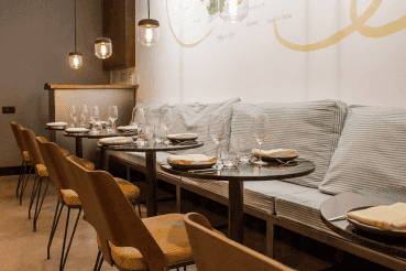 A modern restaurant interior at La Tartareria with wooden chairs, set dining tables, striped cushioned bench seating, and pendant lights.