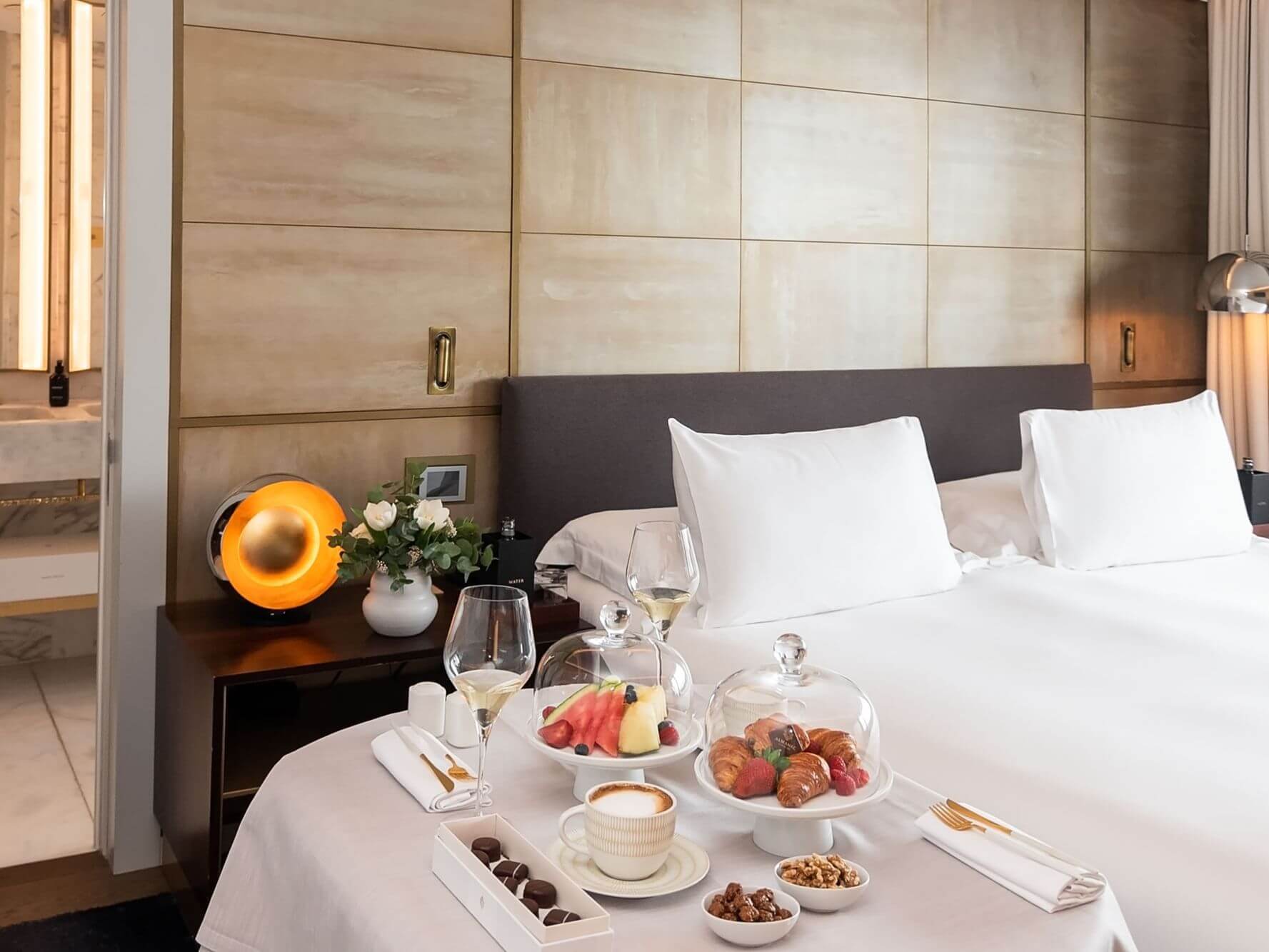 Una suite àtic amb un llit ben fet, una taula parada amb fruita, pastissos, cafè, vi i aperitius, a més d'una tauleta de nit amb una petita làmpada i flors, perfecta per a hostes que busquen luxe a les dues habitacions.