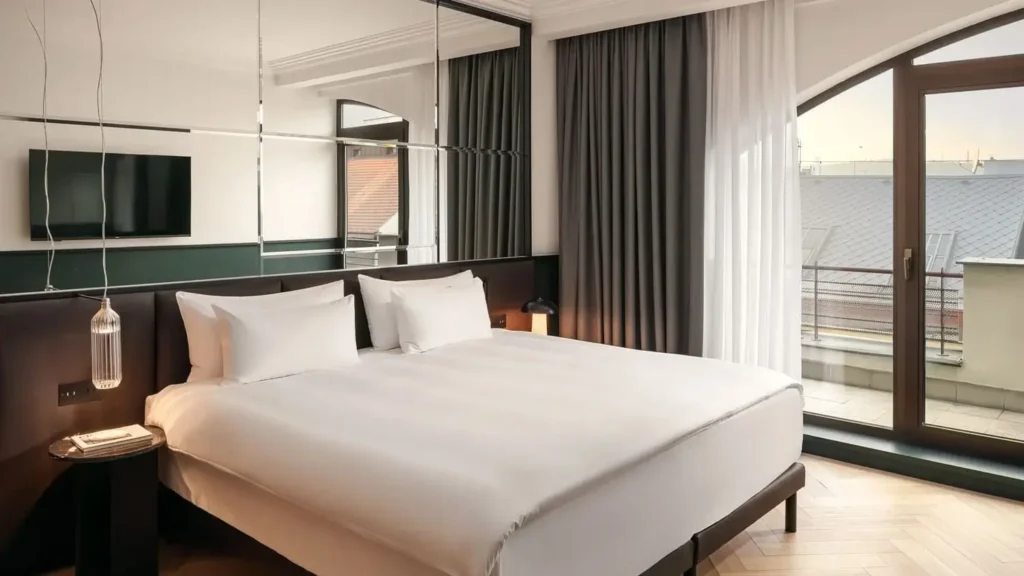 Moderní pokoj Apartmá Executive s velkou postelí, nástěnnou TV, závěsným světlem, skleněnými dveřmi vedoucími na balkon a tmavými závěsy od podlahy až ke stropu.