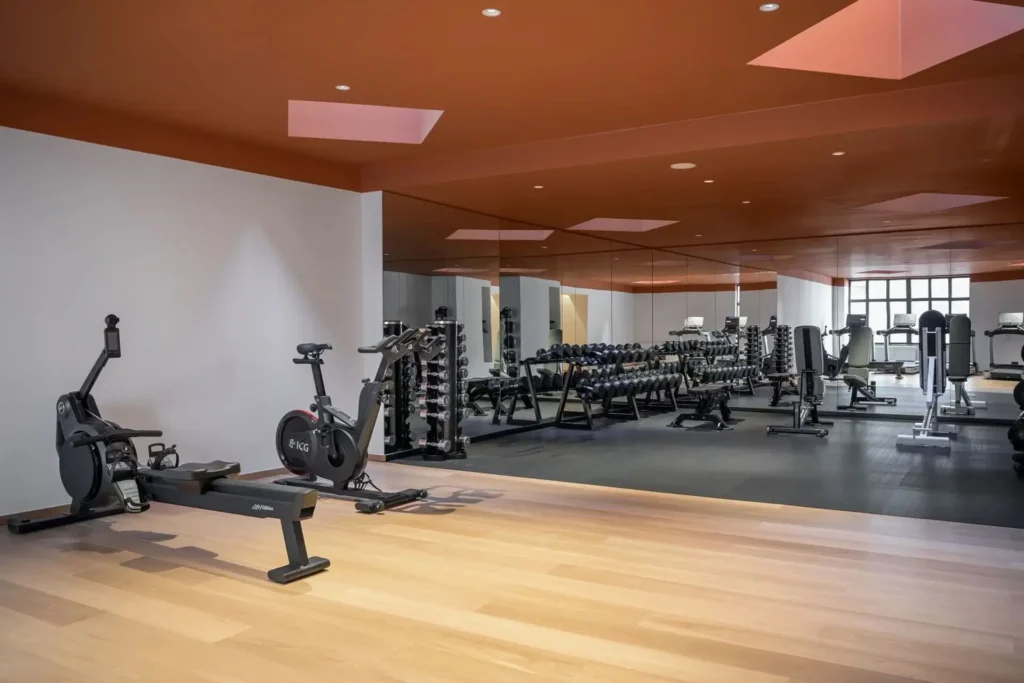 Modern fitness gym with wooden floors, exercise bikes, rowing machines, and a mirrored wall reflecting free weights and strength training equipment—designed to inspire your wellness journey.