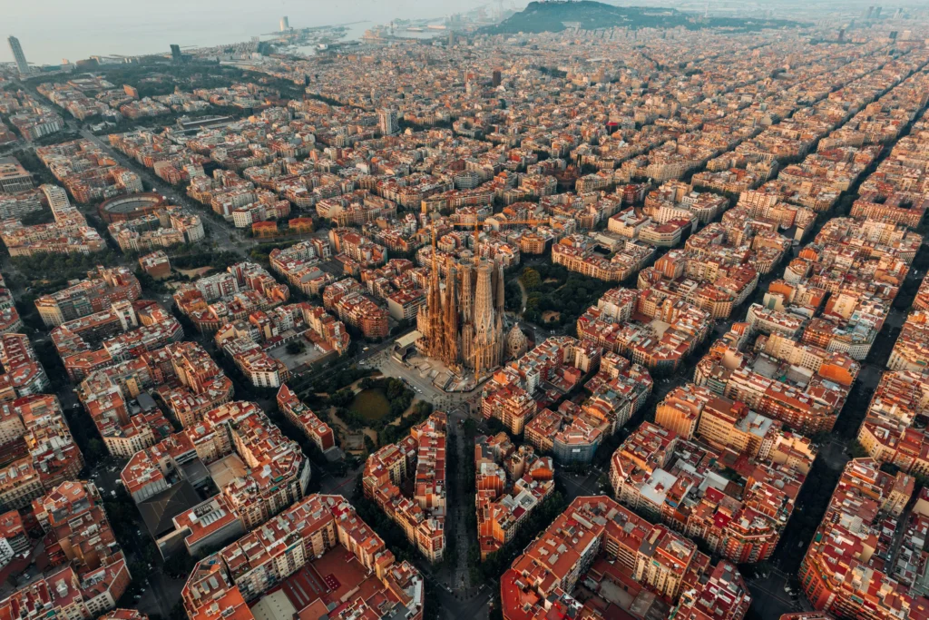 Aerial view of Barcelona’s city grid with the Sagrada Família basilica in the center, L’Auditori Barcelona nearby, all surrounded by densely packed buildings.
