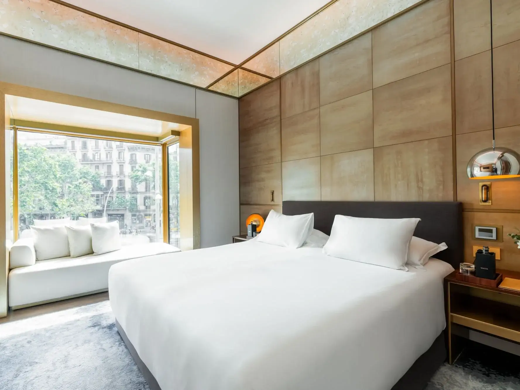 Suite familiar moderna Almanac amb un llit gran, dos coixins blancs, tauletes de nit, un seient a la finestra i una finestra amb vistes als arbres i als edificis de la ciutat.