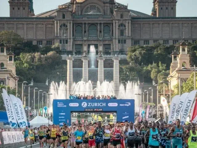 A large group of runners participates in a Zurich marathon event one brisk April morning, with fountains and a grand historic building in the background.