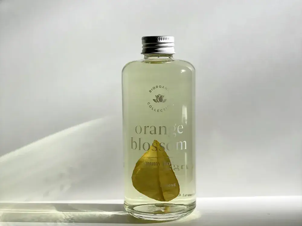 Clear glass bottle labeled "orange blossom," part of Jimmy Boyd fragrances, containing a light liquid and a single dried leaf, with a silver cap, set against a plain white background.