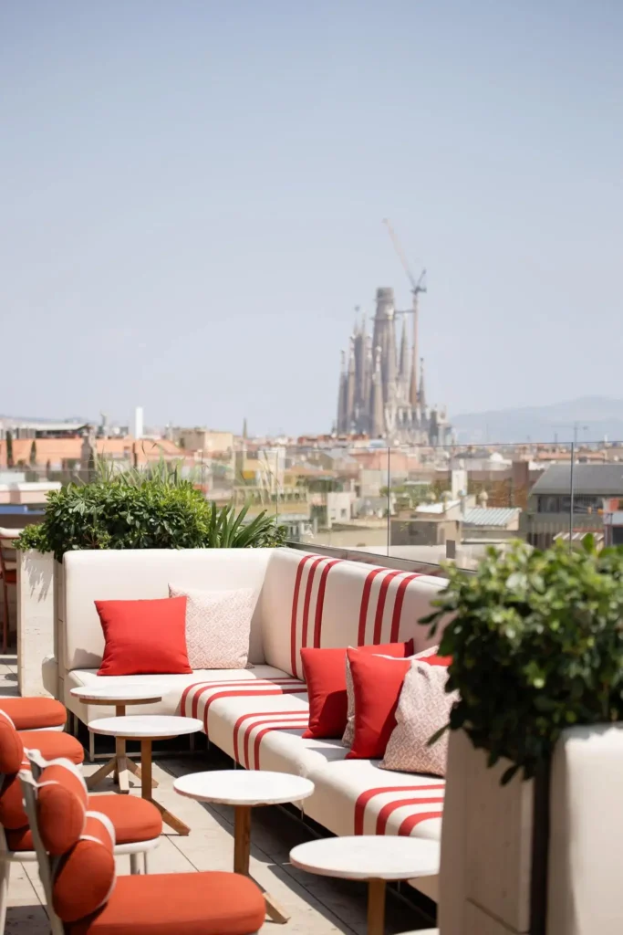 A rooftop terrace at Azimuth Rooftop Bar with red and white striped seating overlooks a cityscape, featuring a large cathedral and a crane in the background.