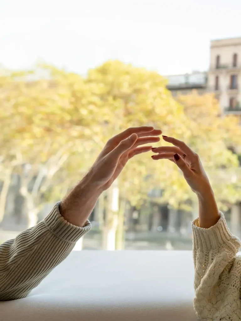 Dues persones amb jerseis s'estenen de la mà l'una cap a l'altra, envoltades d'arbres i edificis borrosos: el moment perfecte per a una Escapada de Tardor.