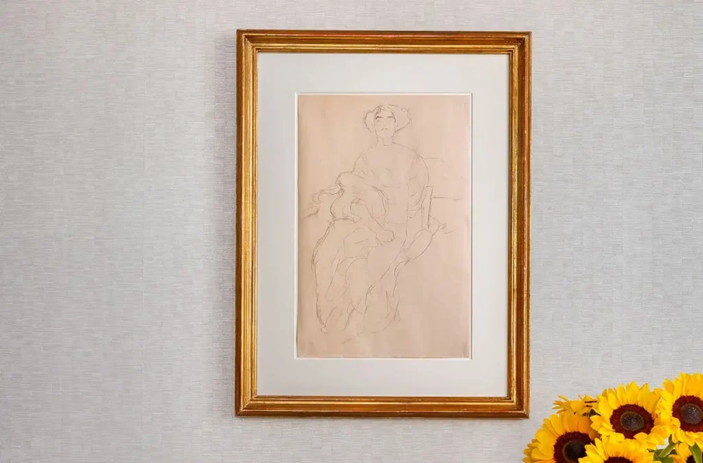 A framed pencil sketch of a seated person hangs on a light-colored wall, with a bouquet of sunflowers visible in the bottom right corner.