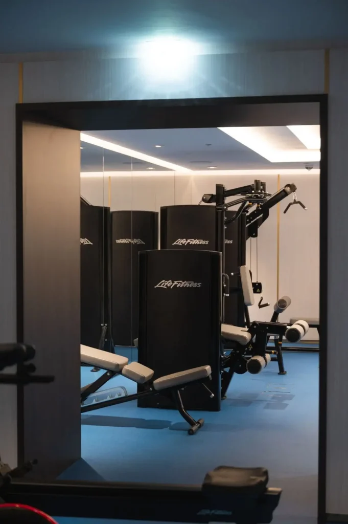 A modern gym room with blue flooring, featuring Life Fitness strength training machines and a bench, offers a dedicated wellness space seen through an open doorway.