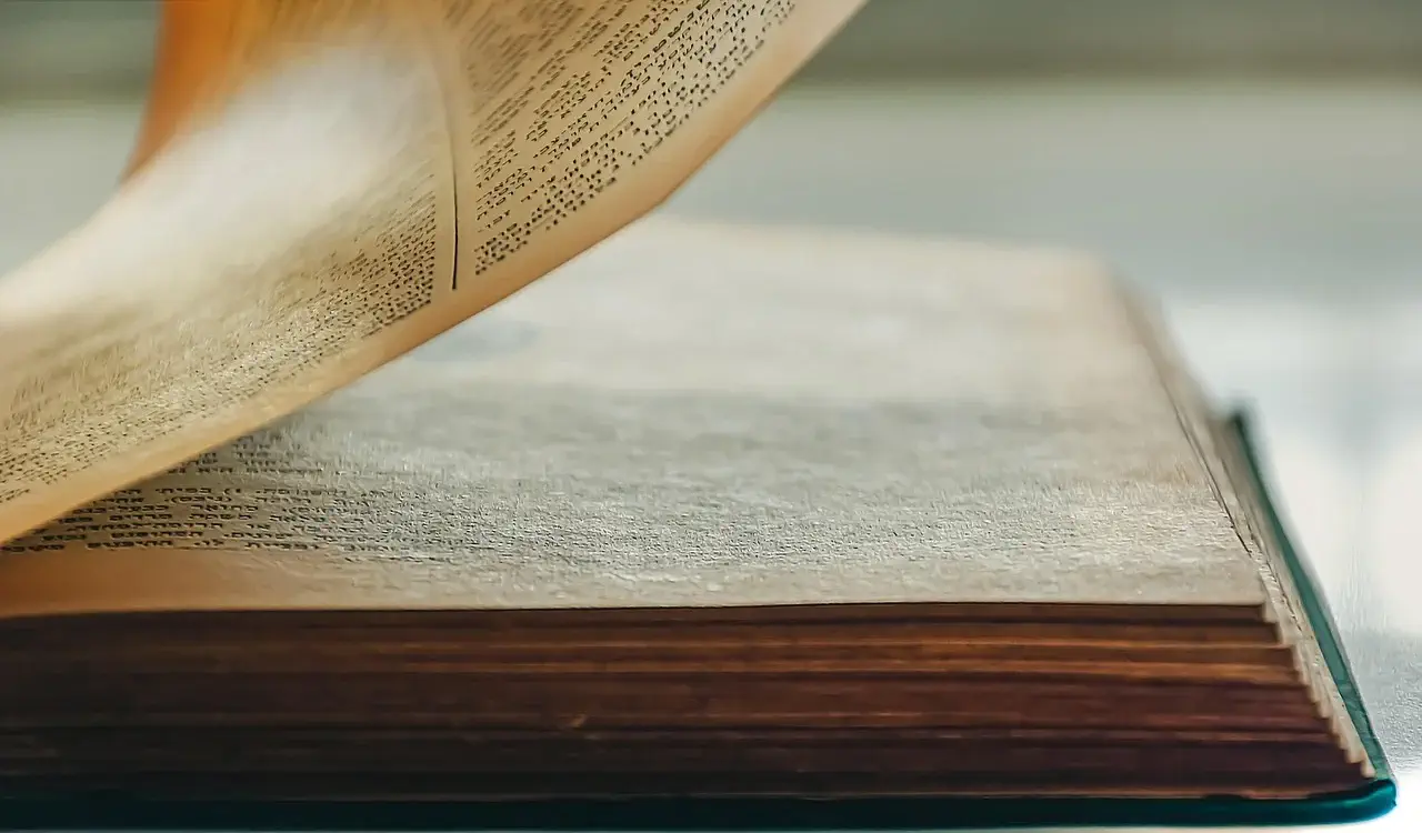 Close-up of an old book with yellowed pages, one page being turned, revealing dense printed text.