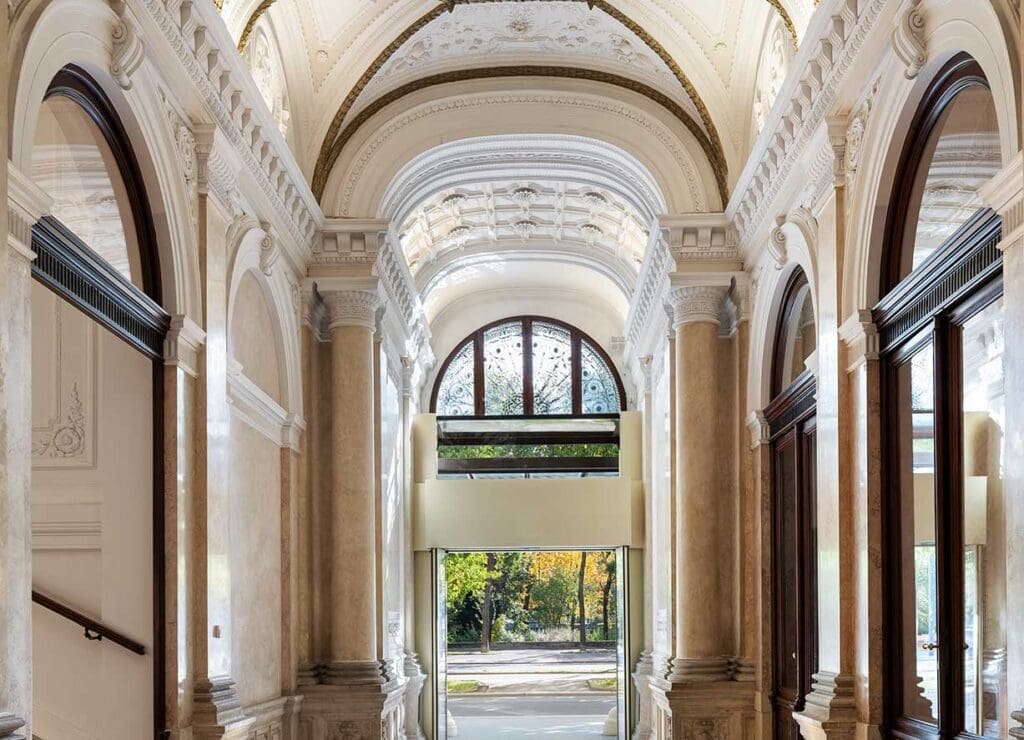 Arched hallway with ornate columns and decorative ceiling, featuring large windows and a view of trees outside—perfect for showcasing your home during the Black Friday offer.