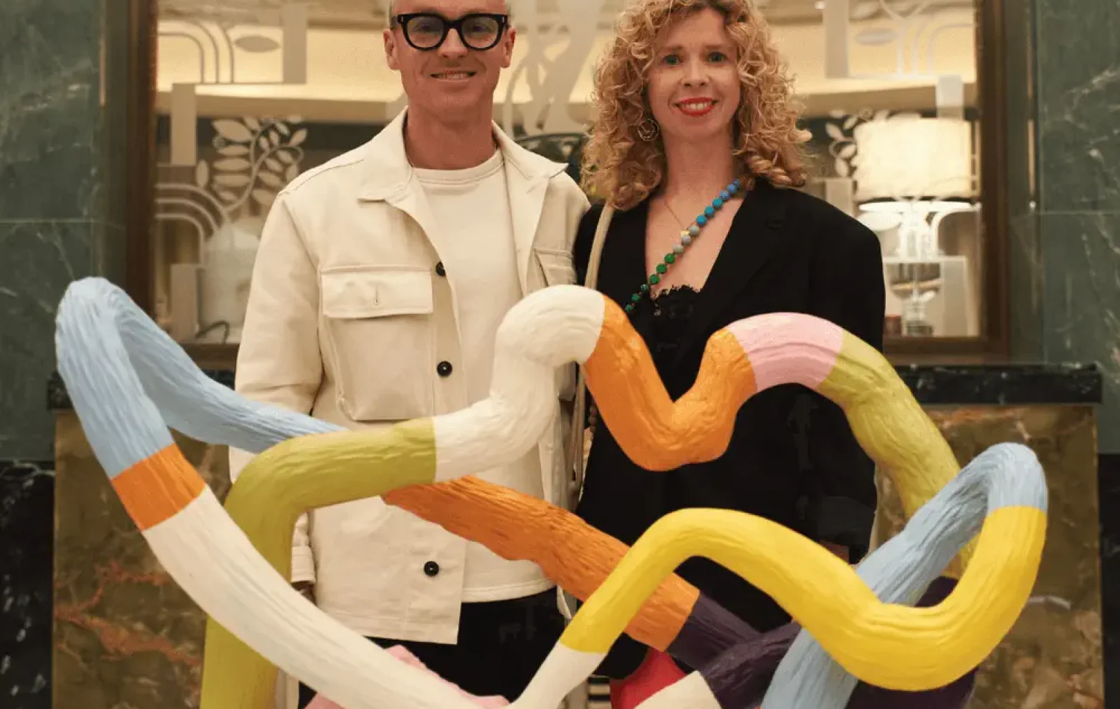 Two people stand indoors behind a colorful abstract sculpture featuring intertwined, ribbon-like shapes, part of the museum’s Signature Tours collection.