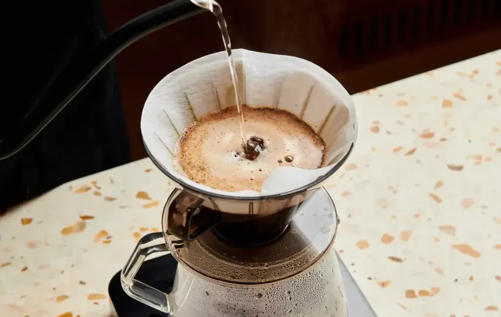 Hot water is being poured from a gooseneck kettle over ground coffee in a filter, using a pour-over coffee maker on a terrazzo countertop—a perfect start before exploring the city with Signature Tours.