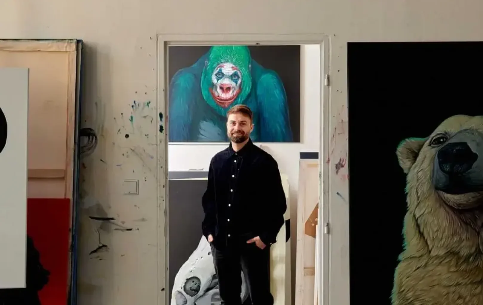 A man stands in an art studio, surrounded by large animal paintings—including a gorilla behind him and a partial bear to his right—offering a glimpse into the creativity behind his Signature Tours.