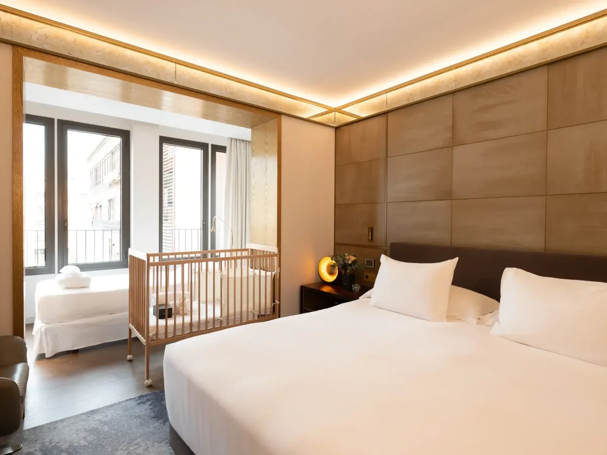 Moderna habitación adaptada con una cama grande, una cuna, una cama individual junto a la ventana y una cálida iluminación. Las ventanas del suelo al techo dejan entrar la luz natural.