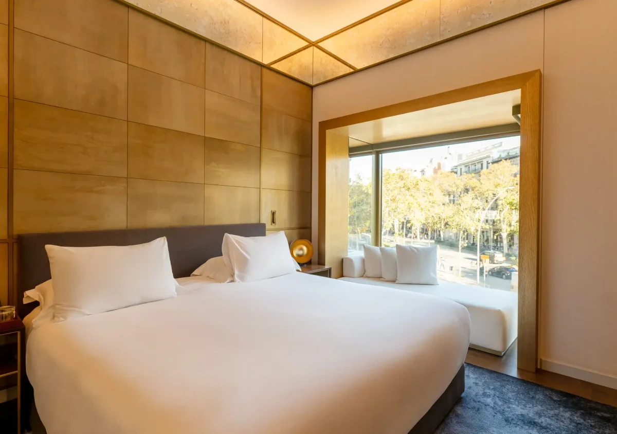 Modern Almanac Zimmer mit einem großen Bett, frischer weißer Bettwäsche, goldgetäfelten Wänden und einem Fensterplatz mit Blick auf eine von Bäumen gesäumte Straße in der Stadt.