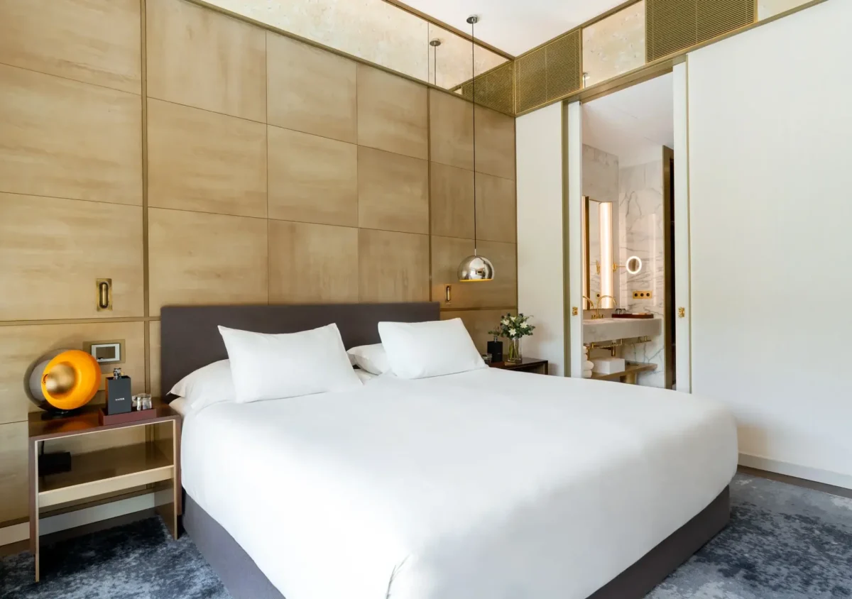 Das moderne Almanaczimmer verfügt über ein ordentlich gemachtes Doppelbett, beige getäfelte Wände, zwei Beistelltische und einen Blick in ein Badezimmer mit Marmoroberflächen. Dieser ruhige Raum verfügt auch über einen Zugang zu einem charmanten Balkon.