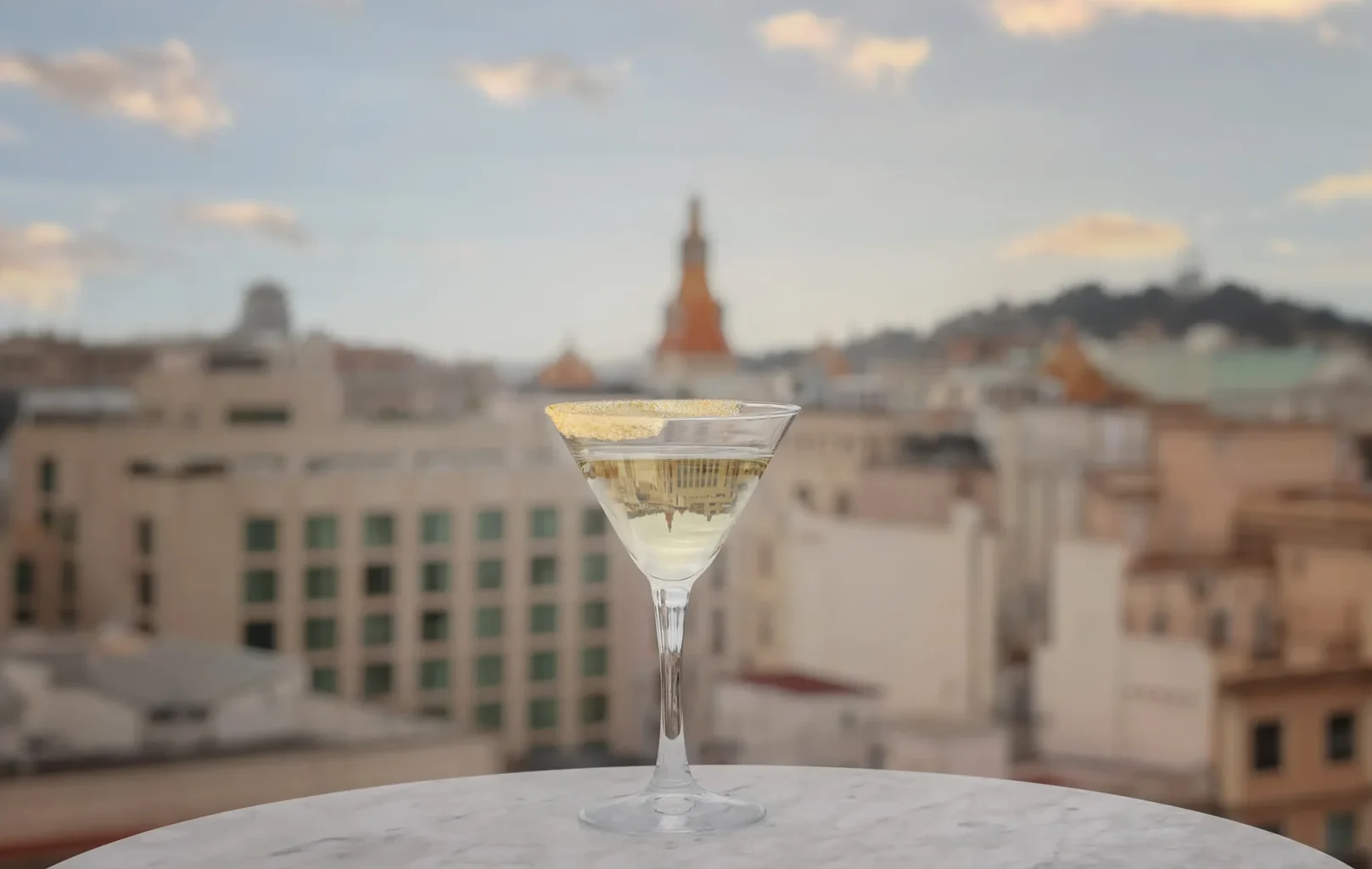 Una copa de vino blanco o champán sobre una mesa de mármol con un paisaje urbano borroso y un cielo nublado de fondo.