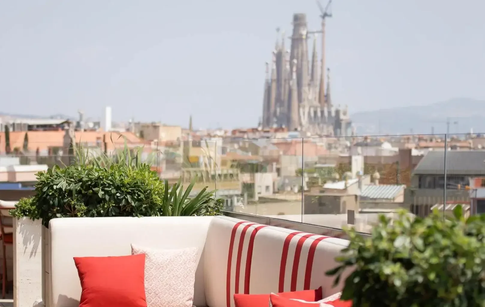 A rooftop terrace at Azimuth Rooftop Bar with red and white striped seating overlooks a cityscape, featuring a large cathedral and a crane in the background.