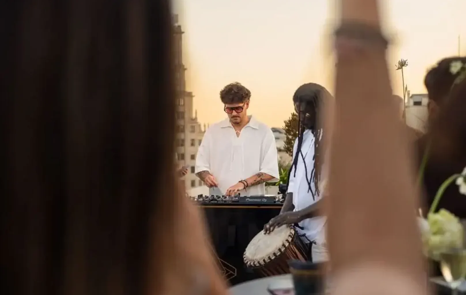 At a Leo Session atop Zenith, a DJ works the mixer while another plays the drum at an outdoor rooftop event, with people visible in the foreground.