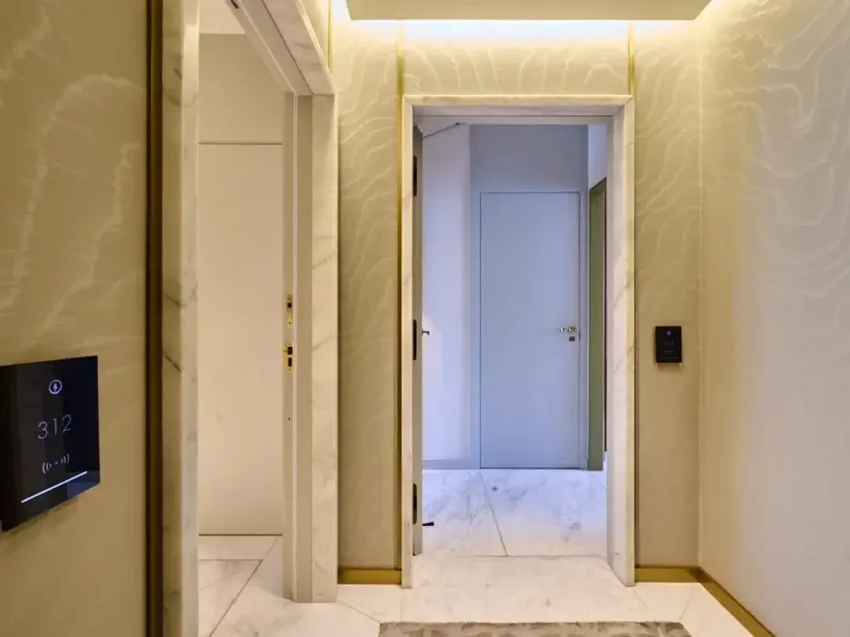 Passadís modern amb terres i parets de marbre clar, una porta oberta que condueix a una altra habitació i un panell de control digital a la paret: perfecte per a una connexió familiar sense problemes a tota la casa.