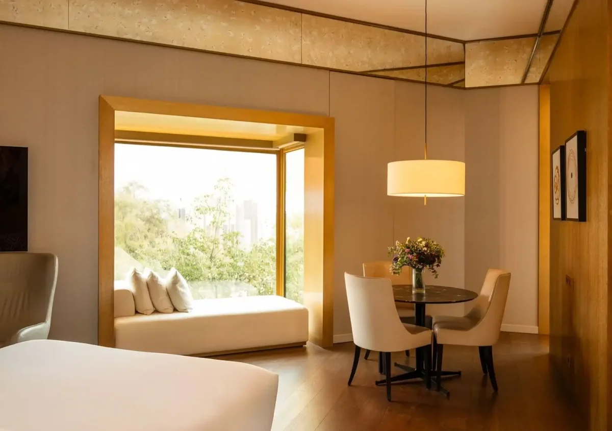 Erleben Sie die Almanac Family Suite: ein modernes Hotelzimmer mit einem Bett, einem Fensterplatz, einem runden Tisch mit vier Stühlen, einer Pendelleuchte und großen Fenstern mit Blick ins Grüne.
