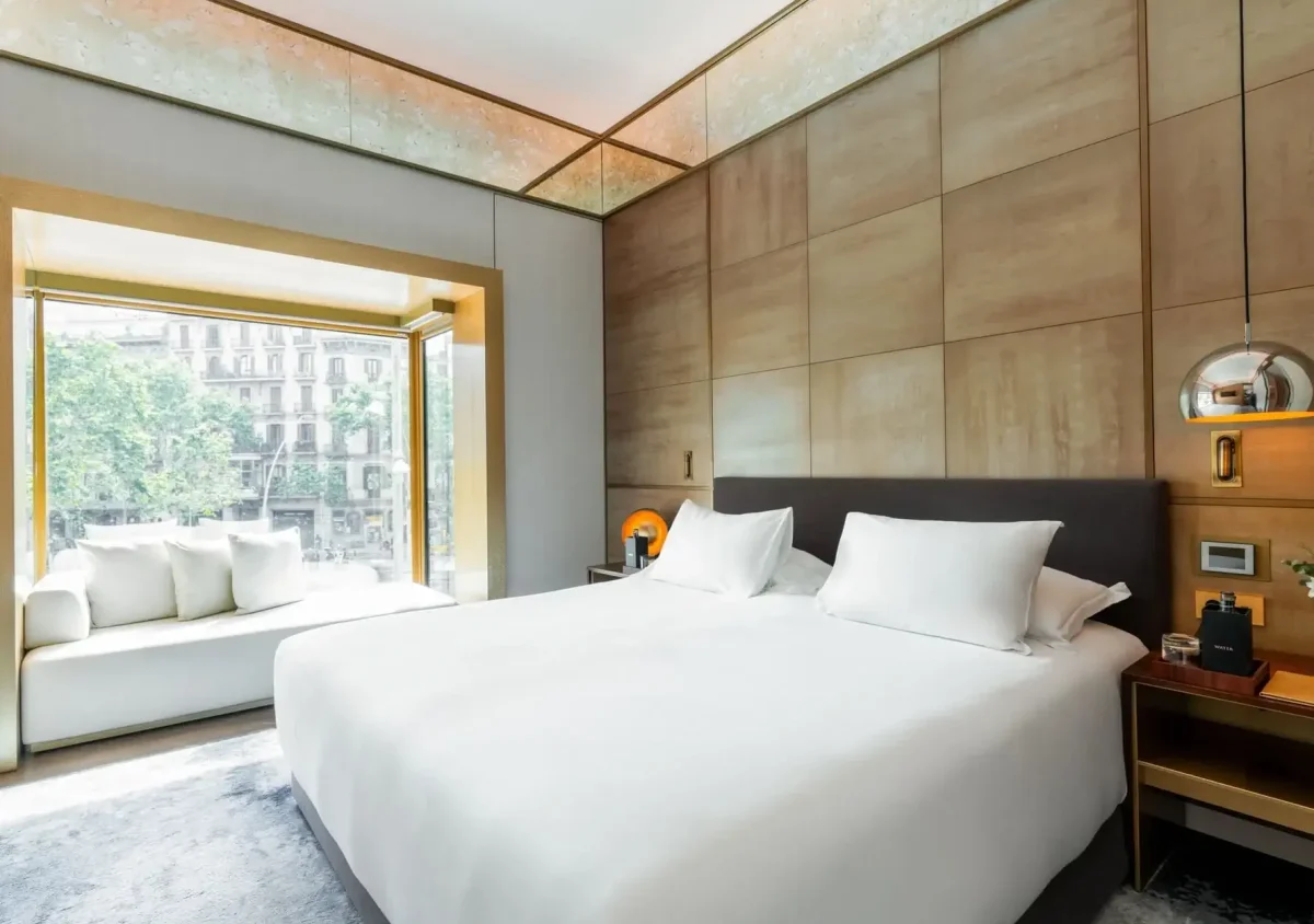 Moderne Familiensuite mit einem großen Bett, zwei Nachttischen, Hängelampen und einem Fensterplatz mit Blick auf eine Stadtlandschaft mit Bäumen.