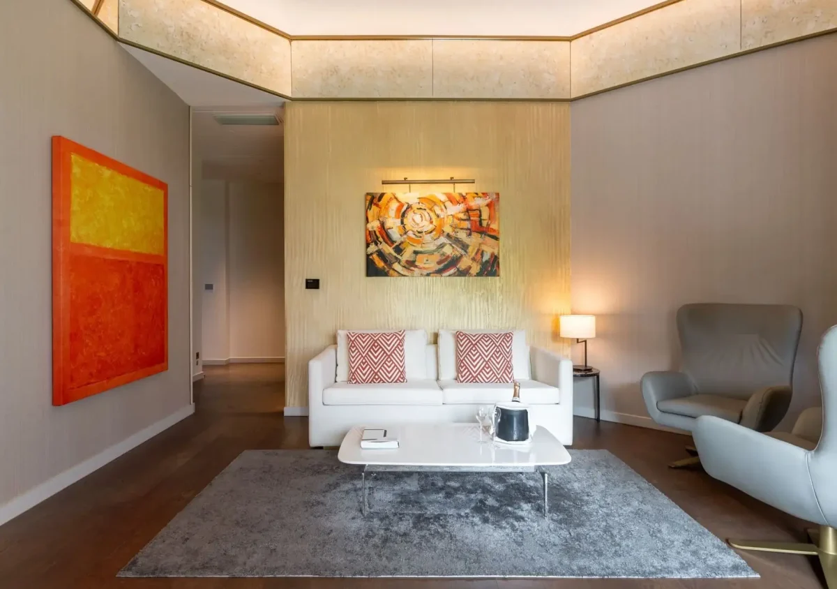 Modernes Wohnzimmer in der Almanac Family Suite mit einem weißen Sofa, gemusterten Kissen, abstrakten Gemälden, einem grauen Sessel, einem Couchtisch und einem grauen Teppich auf Holzboden.