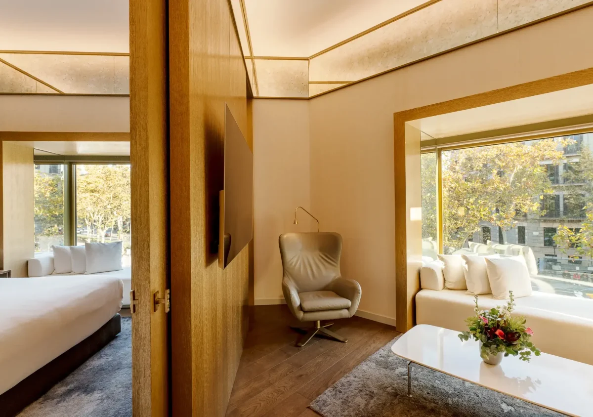 Moderne Almanac Suite mit Bett, Sessel, weißem Sofa, Couchtisch mit Blumen, großen Fenstern und neutralem Dekor - ideal für Gäste, die luxuriösen Komfort in zwei Schlafzimmern suchen.