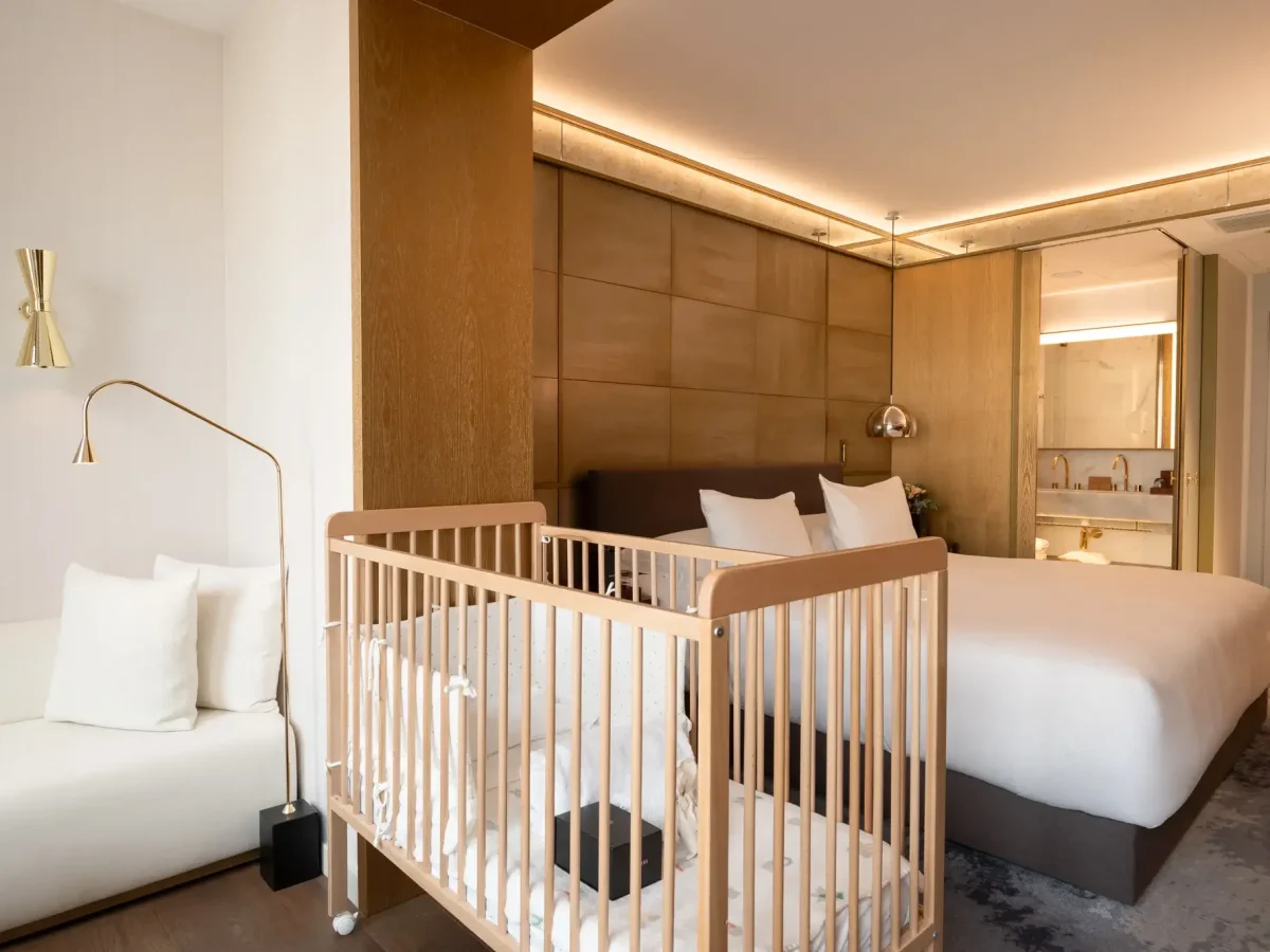 Una Habitació Estudi amb un llit doble, un bressol de fusta, un sofà blanc i un bany modern visible al fons.