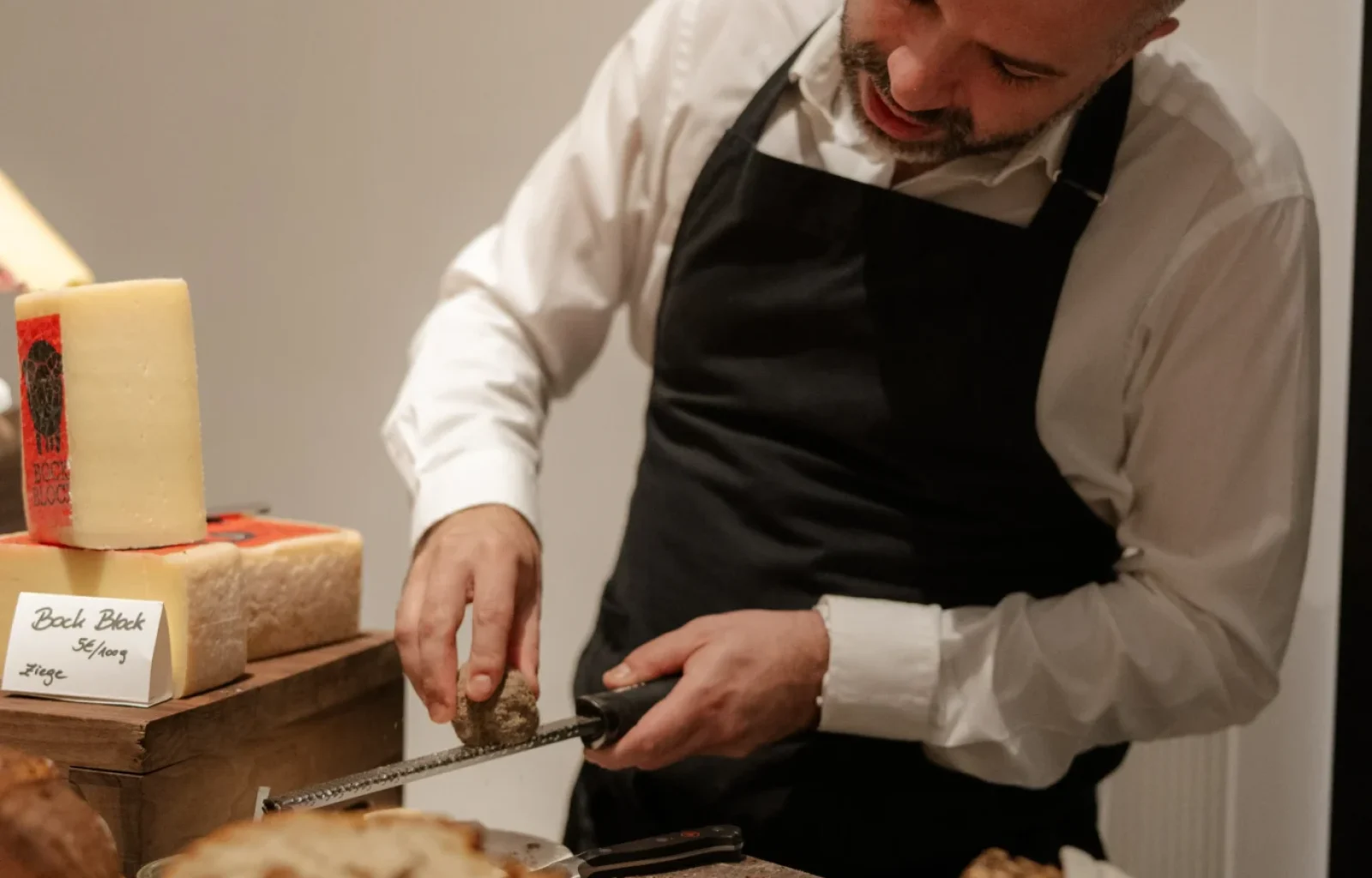 At Donnersmarkt restaurant, a man in a black apron slices bread on a wooden board, surrounded by assorted loaves and a large block of cheese.