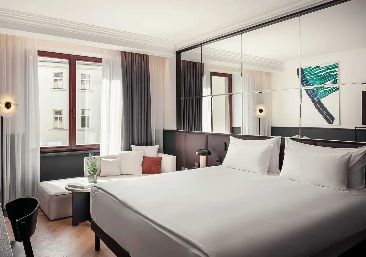 Modern Almanac X hotel room with a large bed, mirrored wall, sofa, two windows with sheer curtains, abstract artwork above the bed, and access to a private balcony.