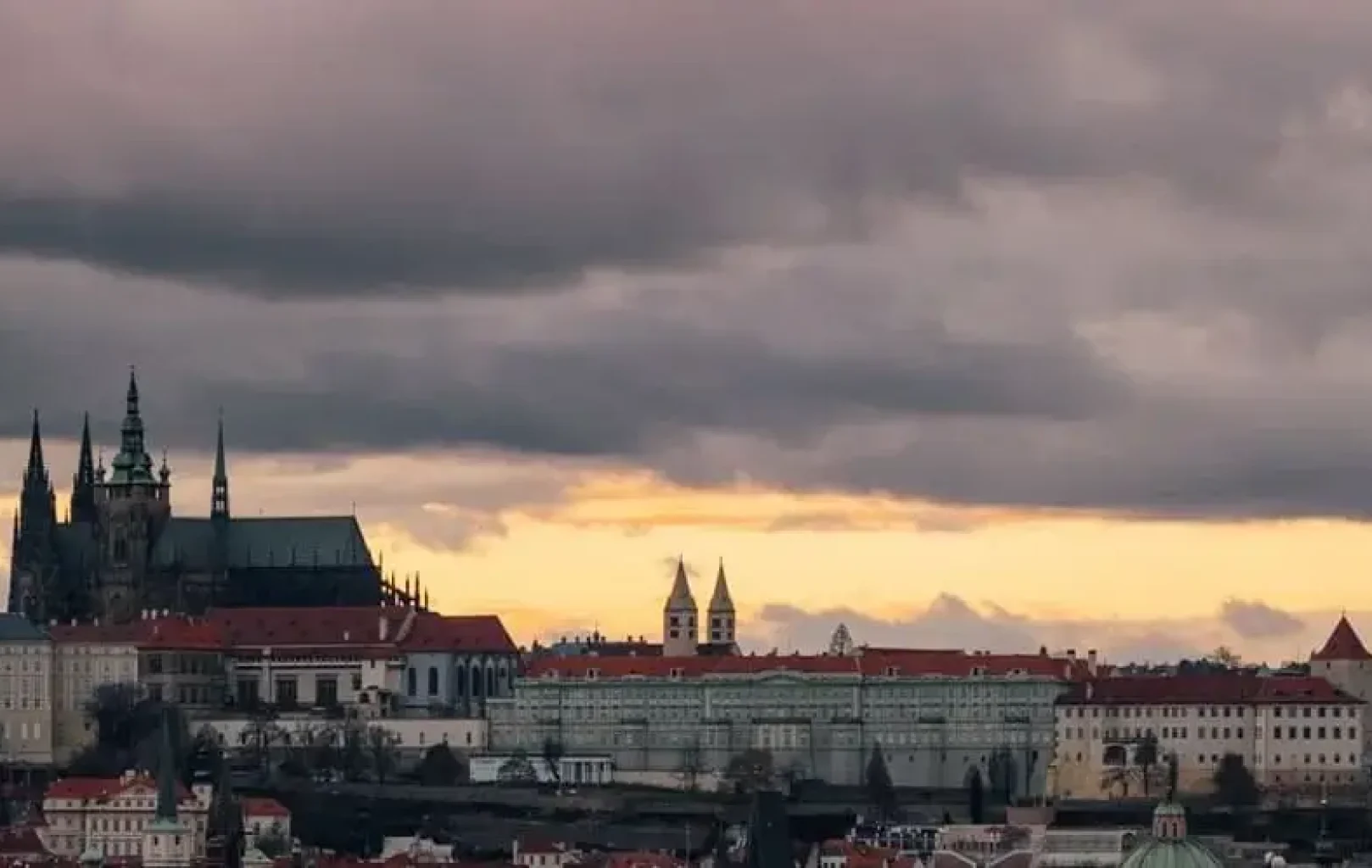 View of Prague Castle and historic buildings under a dramatic cloudy sky at sunset—book 2 nights with our hotel offer and enjoy your third night free.