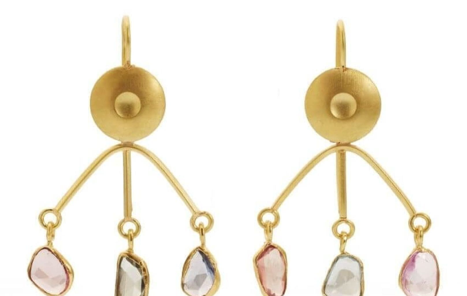 Gold earrings by Assumpta Bou feature a circular stud and three dangling, irregularly shaped gemstones in pink, clear, and blue hues on each earring.