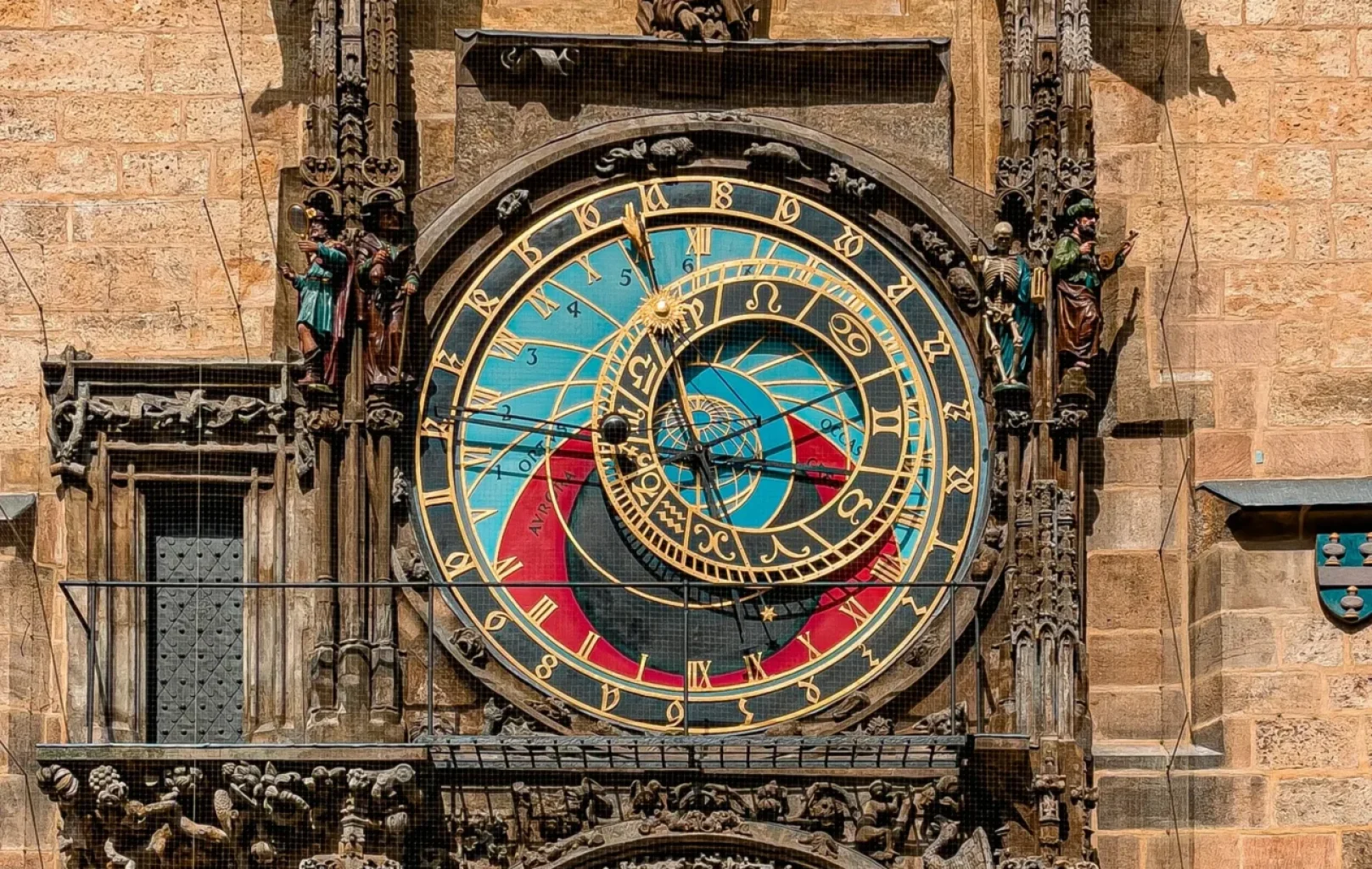 Prague Astronomical Clock on a stone wall, featuring ornate details, two large circular dials with zodiac signs and numbers, and several small statues near the heart of Prague, not far from Wenceslas Square.