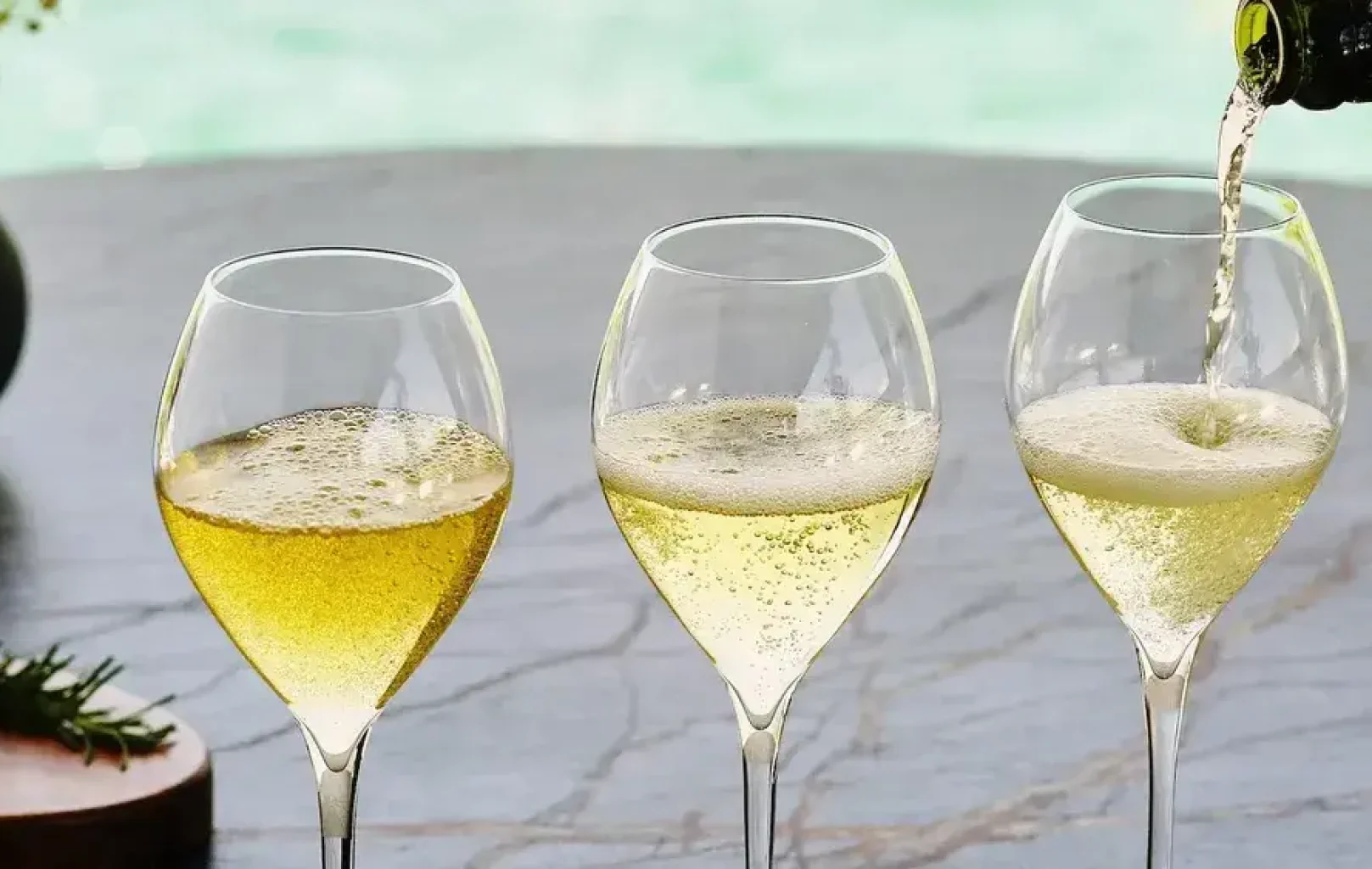 Three wine glasses are filled with sparkling white wine on a table, with a bottle of Corpinnat sparkling wine pouring into the glass on the right—capturing the essence of a memorable winery tour.