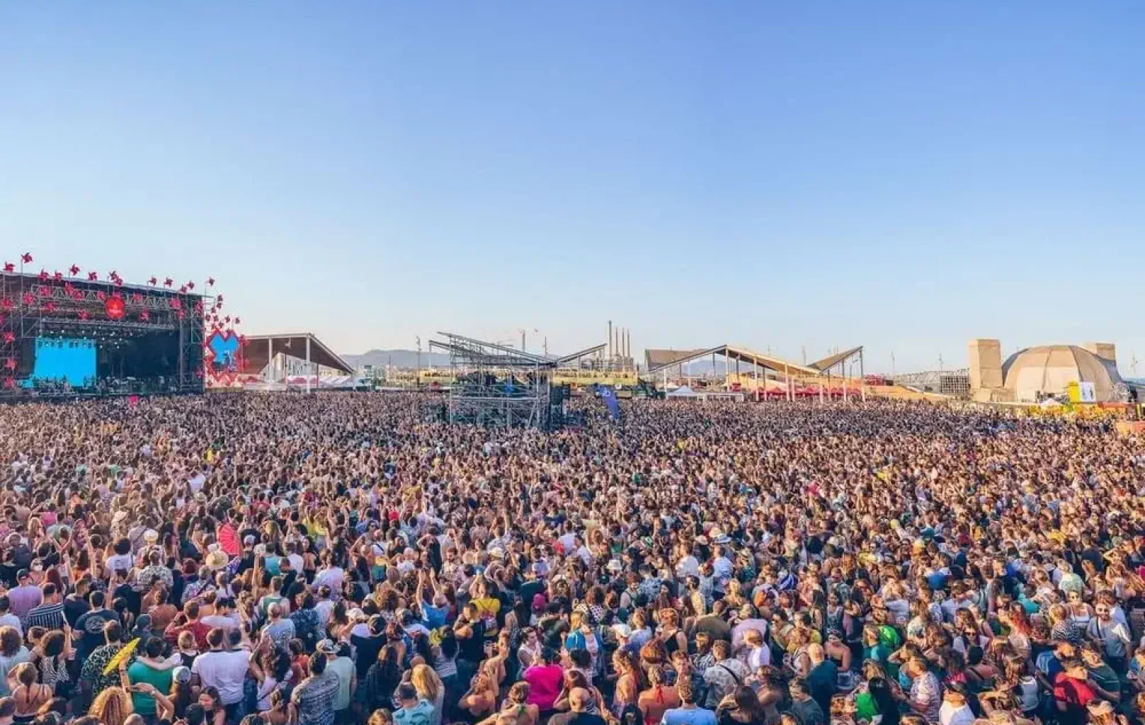 Una gran multitud de persones es va reunir a l'aire lliure davant d'un escenari en un festival de música sota un cel blau clar, gaudint de l'energia vibrant de les celebracions de Juny i Juliol.