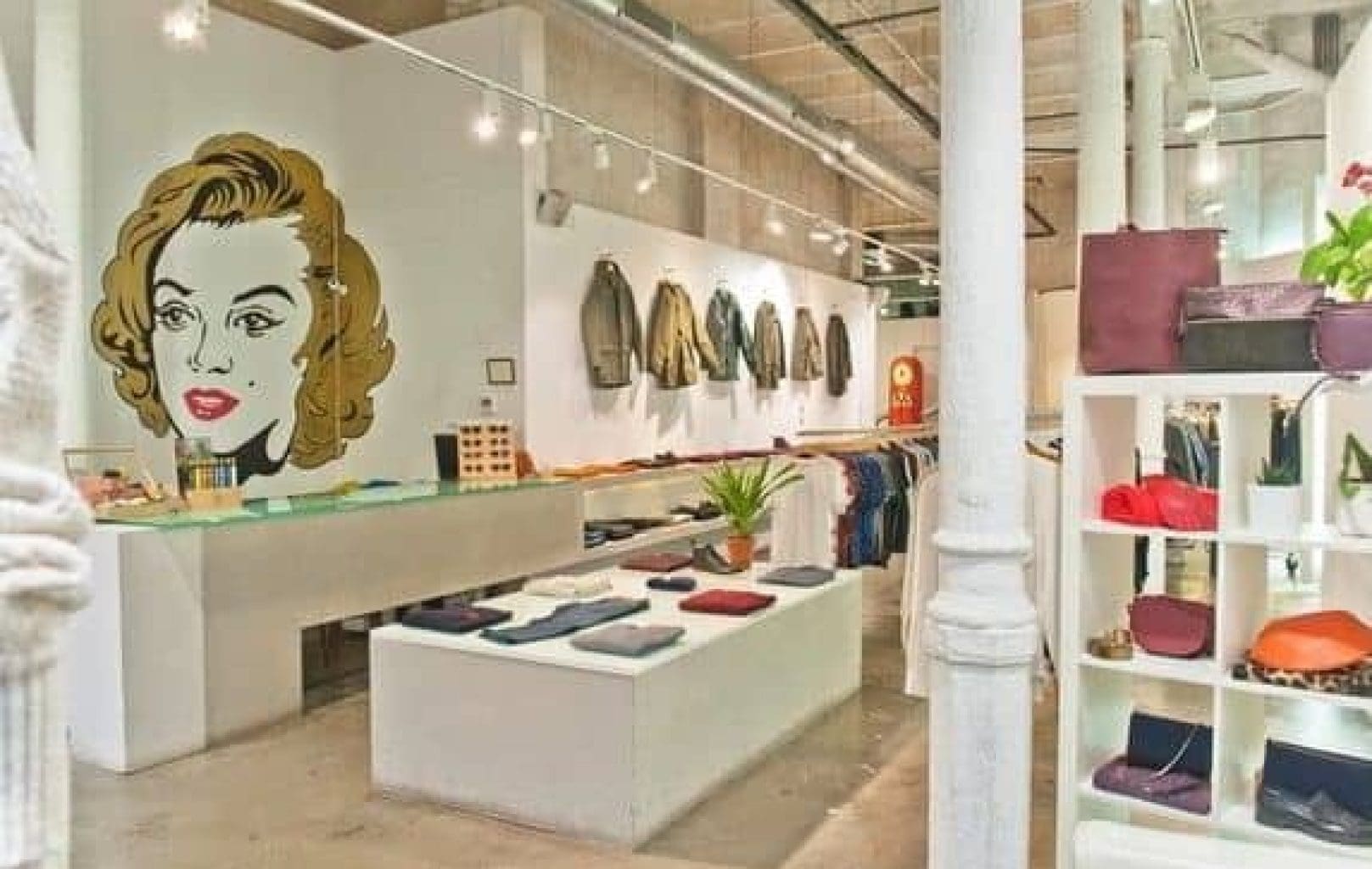 Modern boutique Iguapop Shop with clothing, bags, and accessories displayed neatly; large wall art of a woman's face is featured on the left wall.