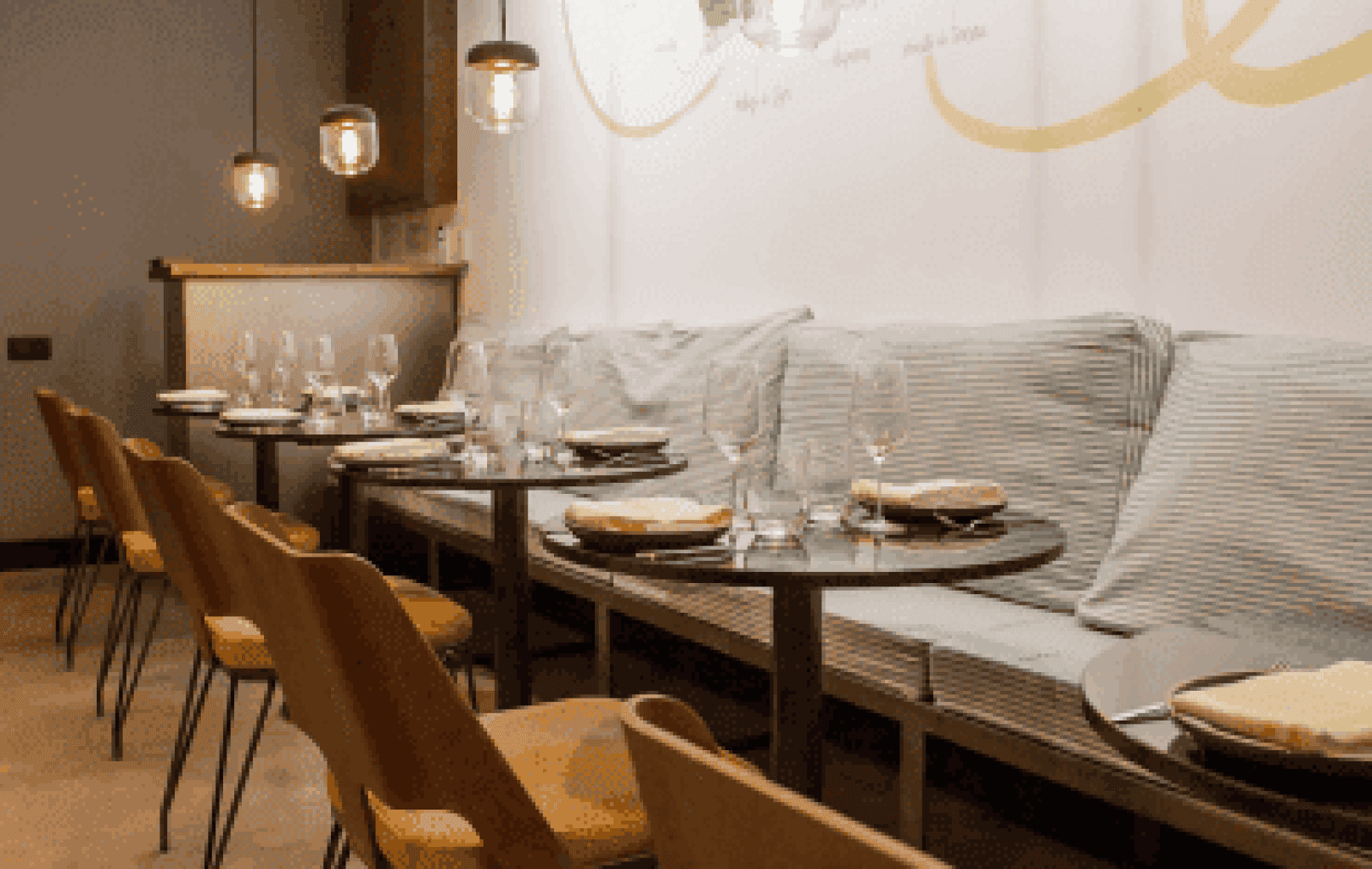 A modern restaurant interior at La Tartareria with wooden chairs, set dining tables, striped cushioned bench seating, and pendant lights.