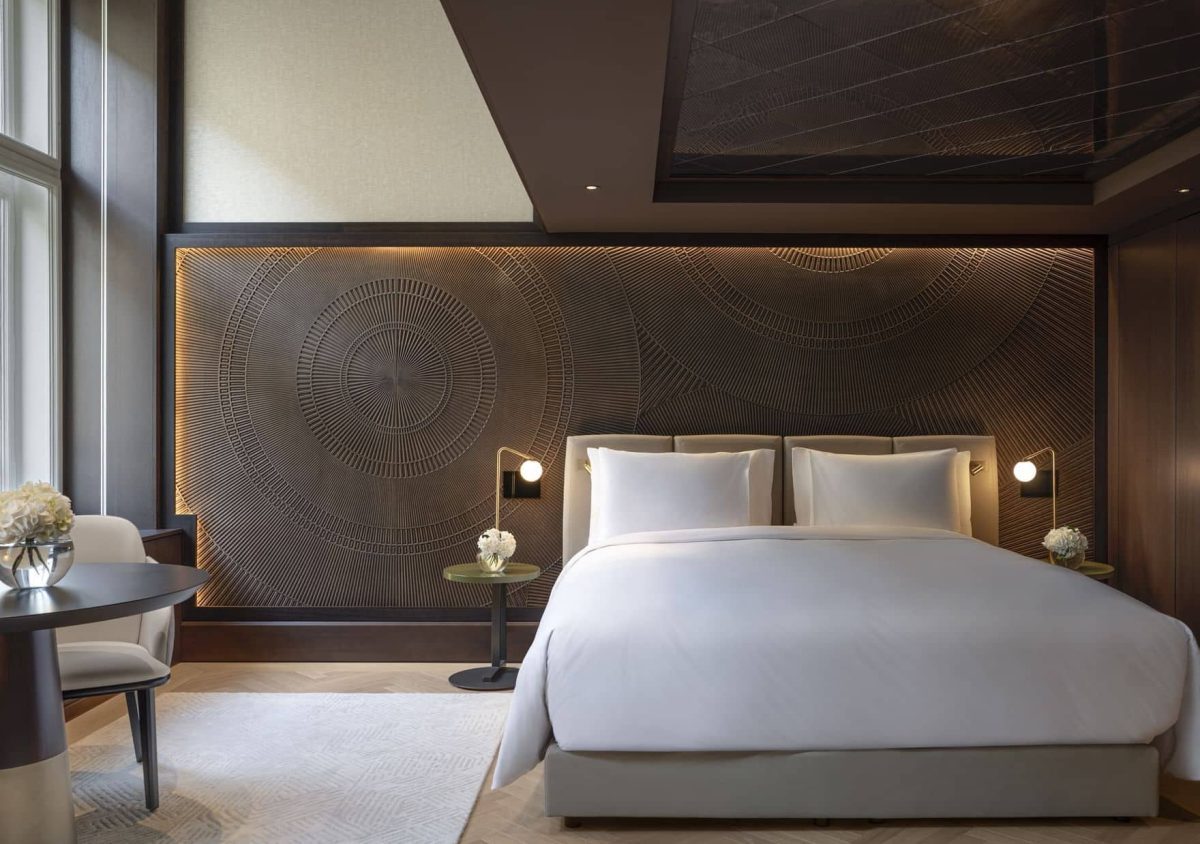 Modern Almanac Deluxe hotel bedroom with a large bed, contemporary wall art, bedside lamps, a small round table with chairs, and floor-to-ceiling windows letting in natural light.