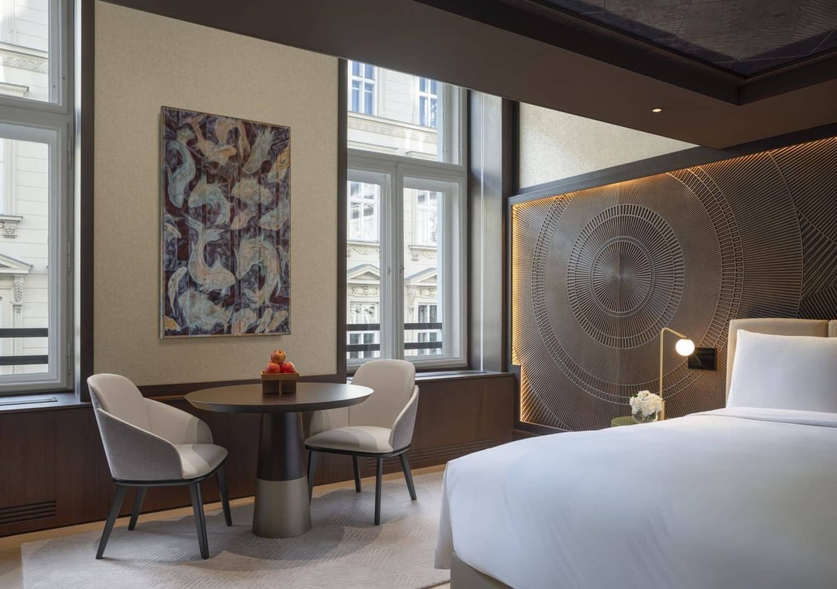 Modern Almanac Deluxe hotel room with a large bed, round table and chairs, wall art, decorative headboard, and two windows. Natural light fills the space.