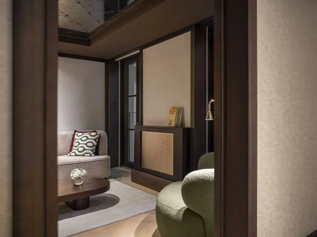 Blick in ein modernes, neutral gehaltenes Familienzimmer mit Sofa, gemustertem Kissen, rundem Couchtisch, grünem Sessel und einer kleinen Vase mit weißen Blumen - perfekt zum Entspannen in der Nähe von zwei Schlafzimmern.