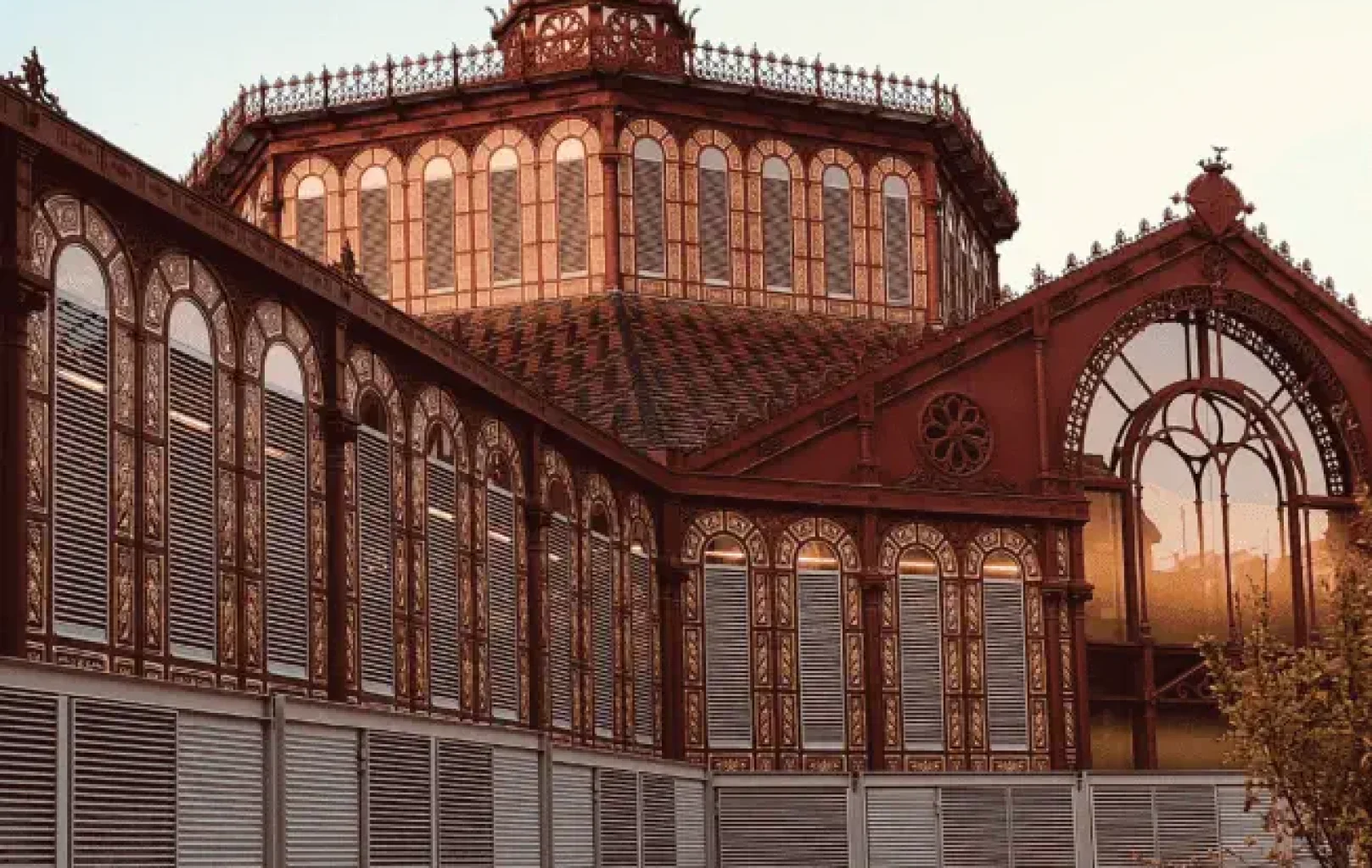 A historic Barcelona building with intricate ironwork and arched windows reflects warm light; the lower section features modern metal panels, inviting you to savour the earth’s unique blend of old and new.