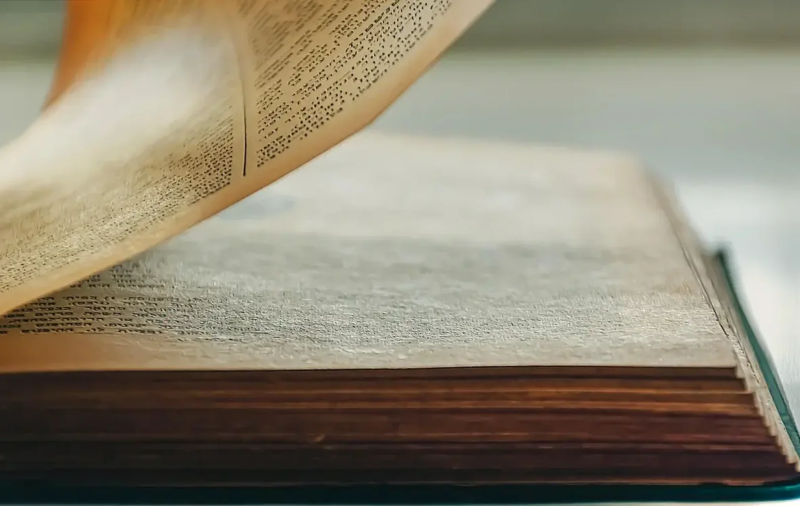 Close-up of an old book with yellowed pages, one page being turned, revealing dense printed text.