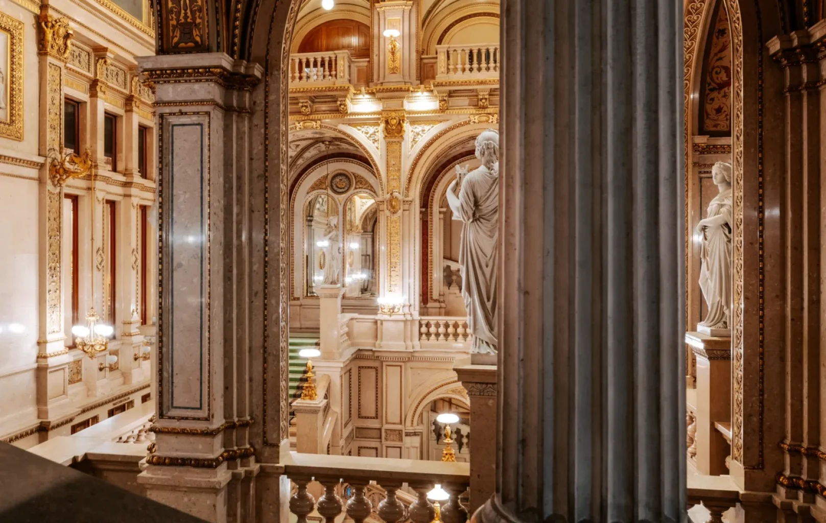 View of an ornate interior with marble columns, arched ceilings, decorative details, and classical statues in the grand Vienna State Opera, one of the most impressive Vienna attractions.